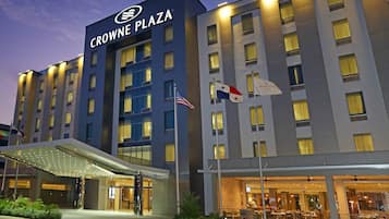 Un hotel con un llamativo letrero 'CROWNE PLAZA', varias banderas y una entrada bien iluminada.