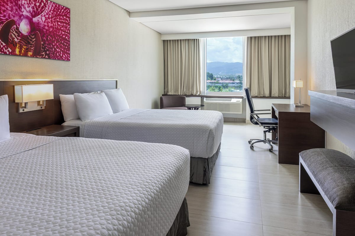 Una habitación de hotel con dos camas, un escritorio, una silla y un televisor.