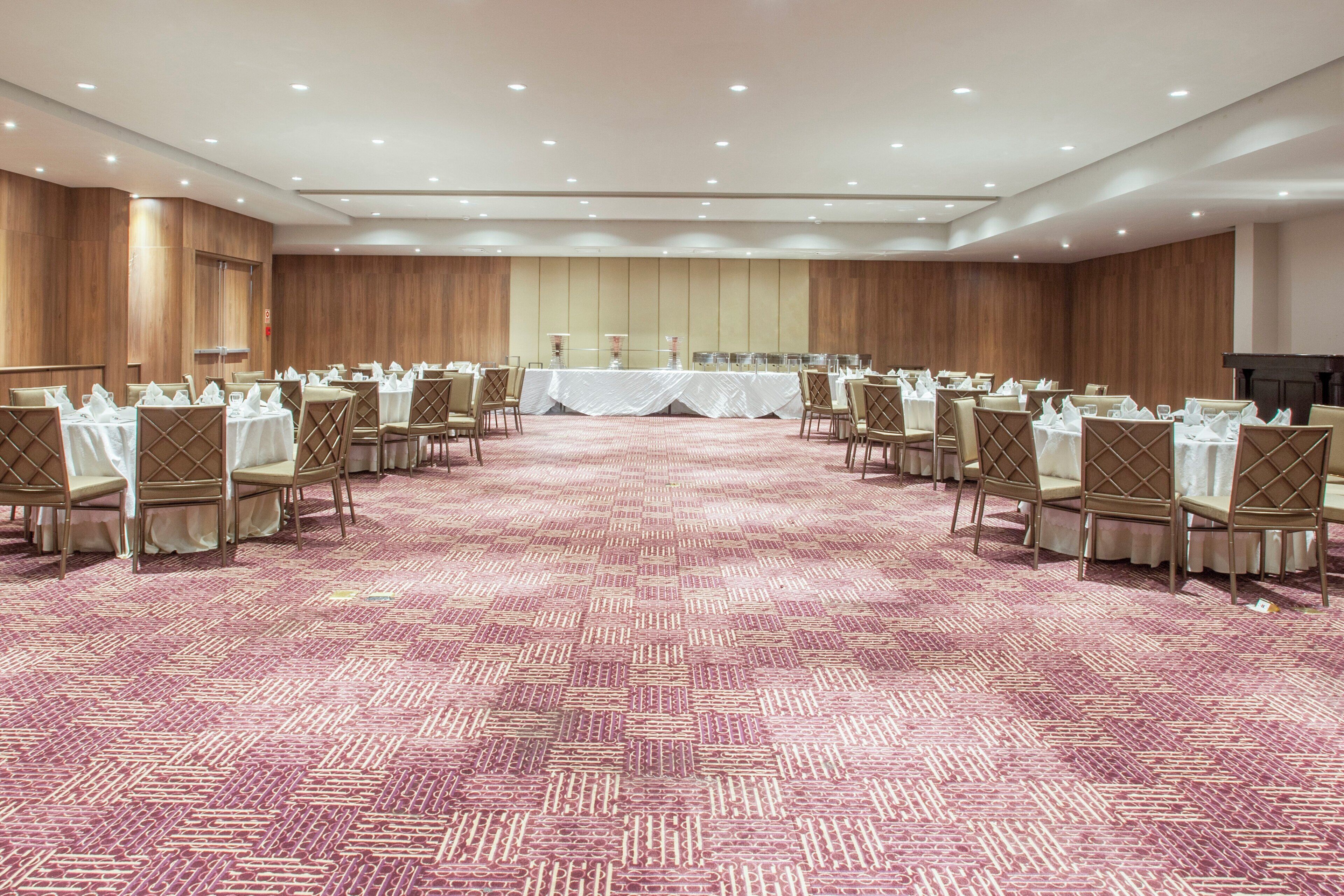 A conference room with rows of tables and chairs, a patterned carpet, and wooden paneling on the walls.