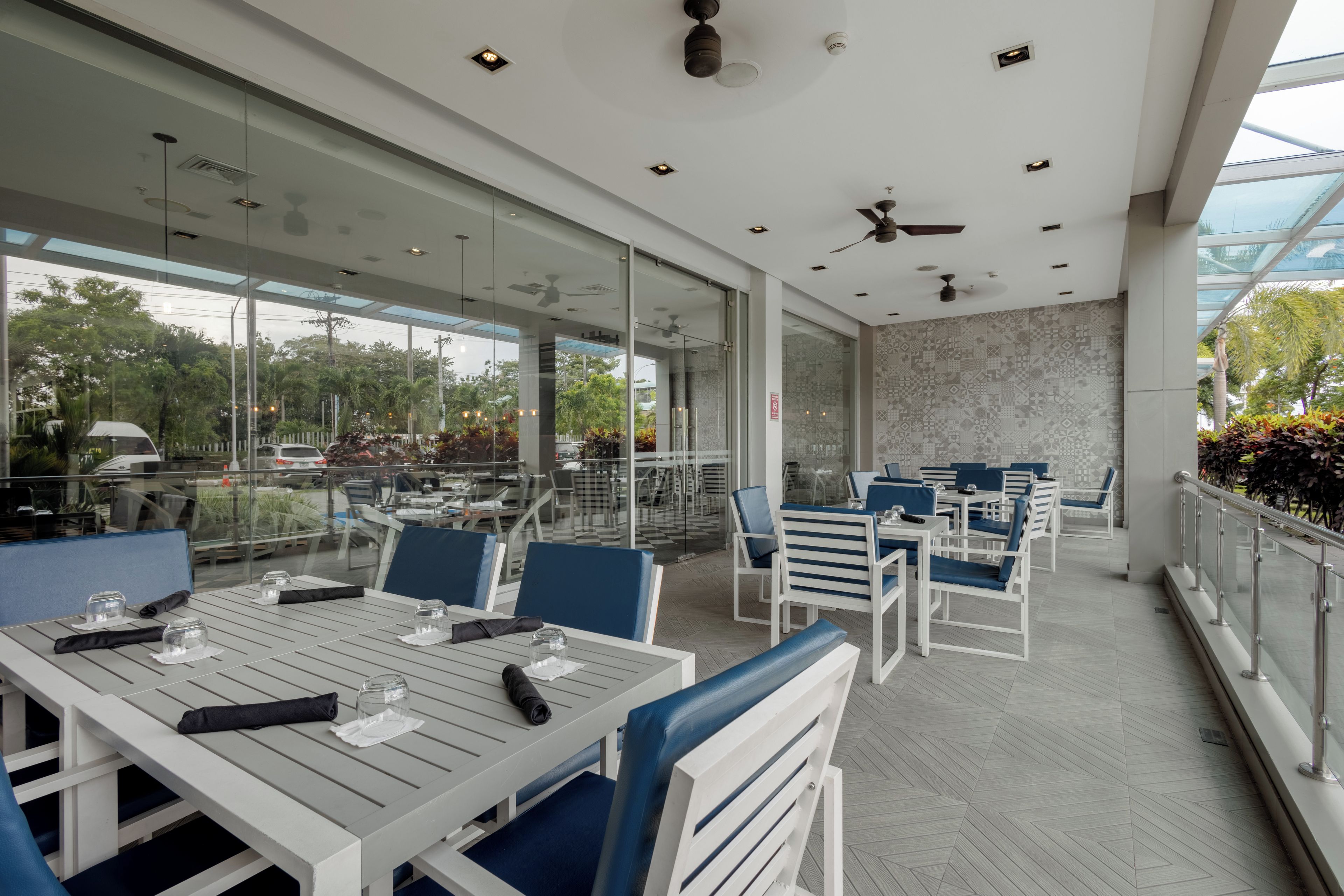 Un restaurant doté d’une terrasse, de murs en verre et de ventilateurs de plafond.