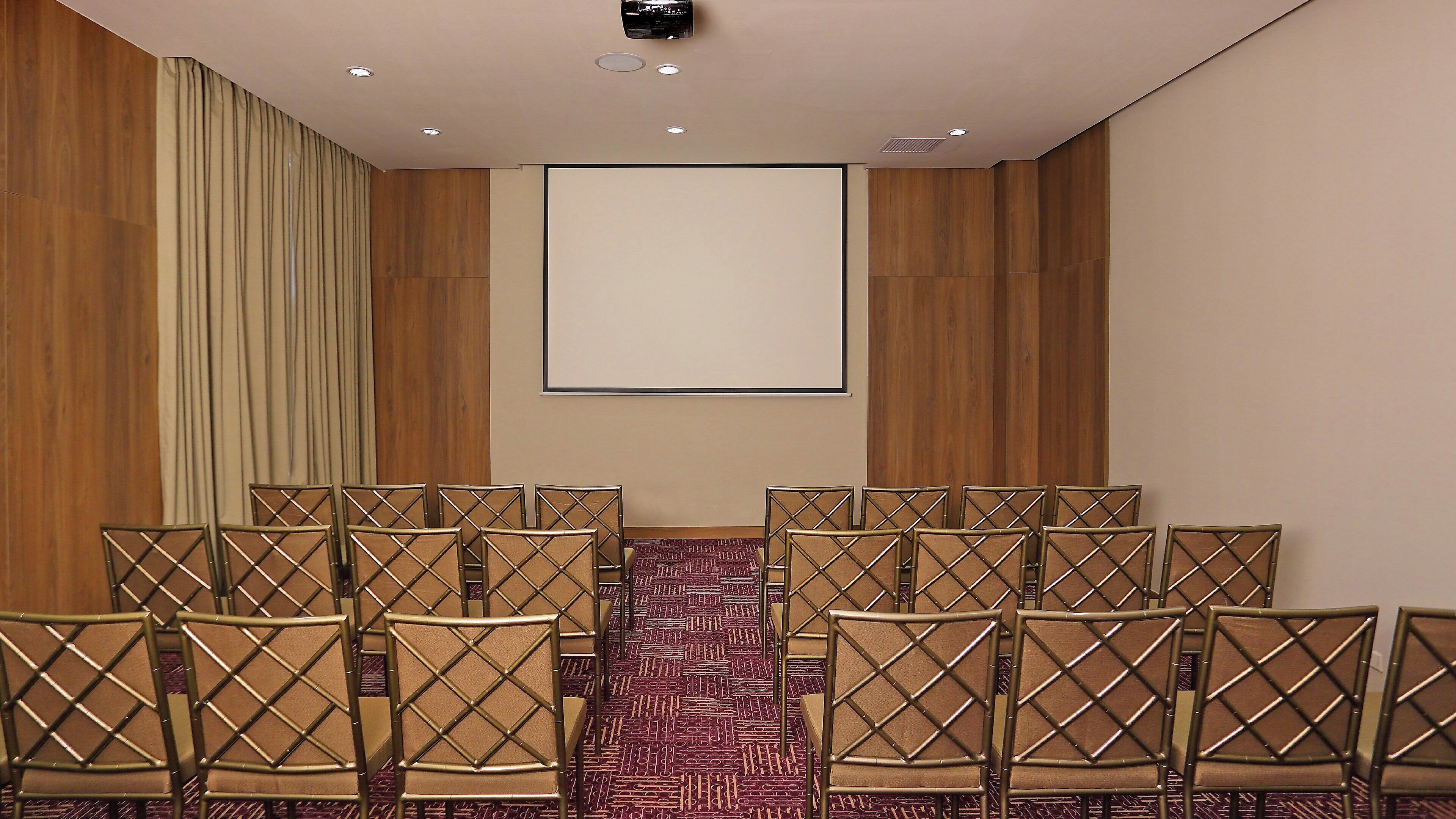 Un salón de conferencias con una pantalla grande, paredes de paneles de madera y filas de sillas.