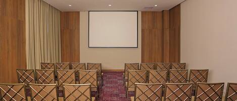 Un salón de conferencias con una pantalla grande, paredes de paneles de madera y filas de sillas.