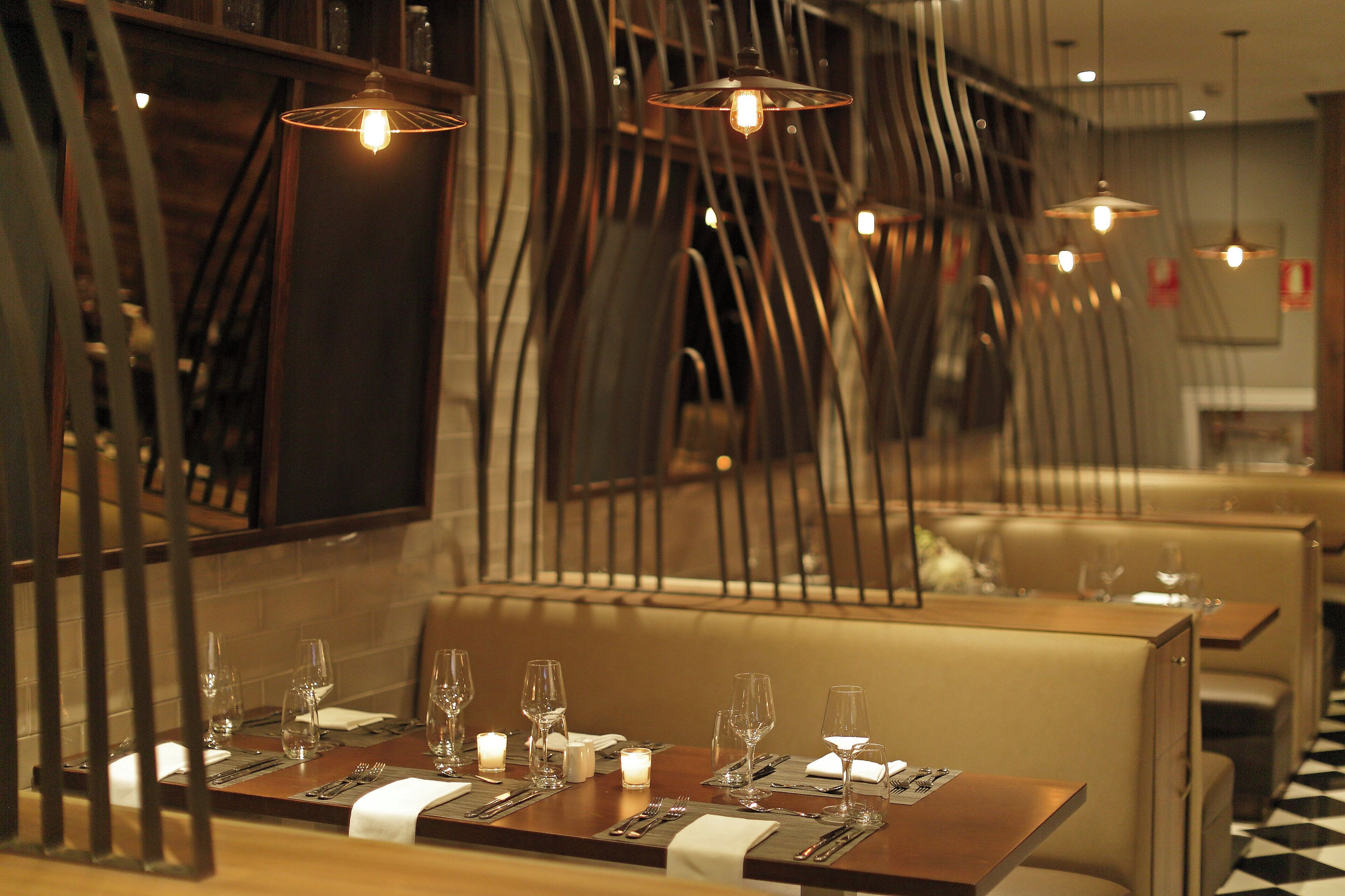 Ein Restaurantinneres mit einem für zwei Personen gedeckten Tisch, mit Kerzen, Besteck und Gläsern.