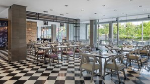 Un restaurante moderno con suelo de cuadros, sillas de madera y ventanas amplias que dan a zonas verdes.