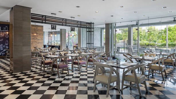 Un restaurante moderno con suelo de cuadros, sillas de madera y ventanas amplias que dan a zonas verdes.