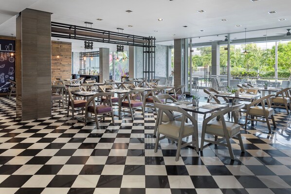 Un restaurante moderno con suelo de cuadros, sillas de madera y ventanas amplias que dan a zonas verdes.