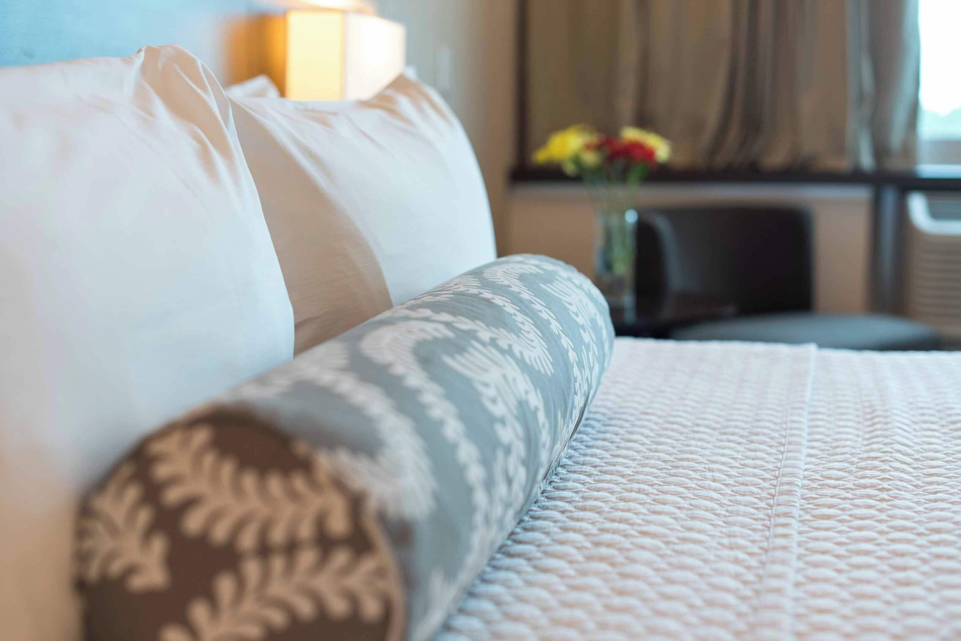 A hotel room with a bed, pillows, a bedside table, and a vase with flowers.