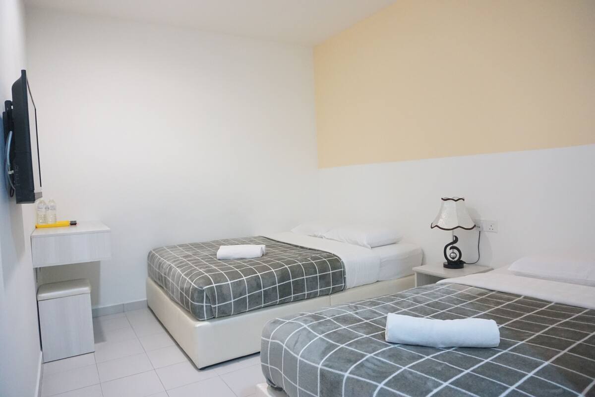 Een hotelkamer met twee bedden, een klein bureau, een lamp en een televisie aan de muur.