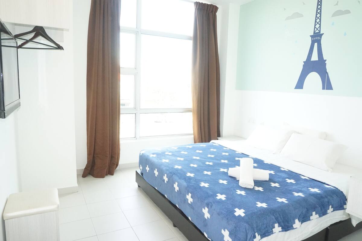 Een hotelkamer met een bed, een raam met gordijnen, een tv aan de muur en een schilderij van de Eiffeltoren.