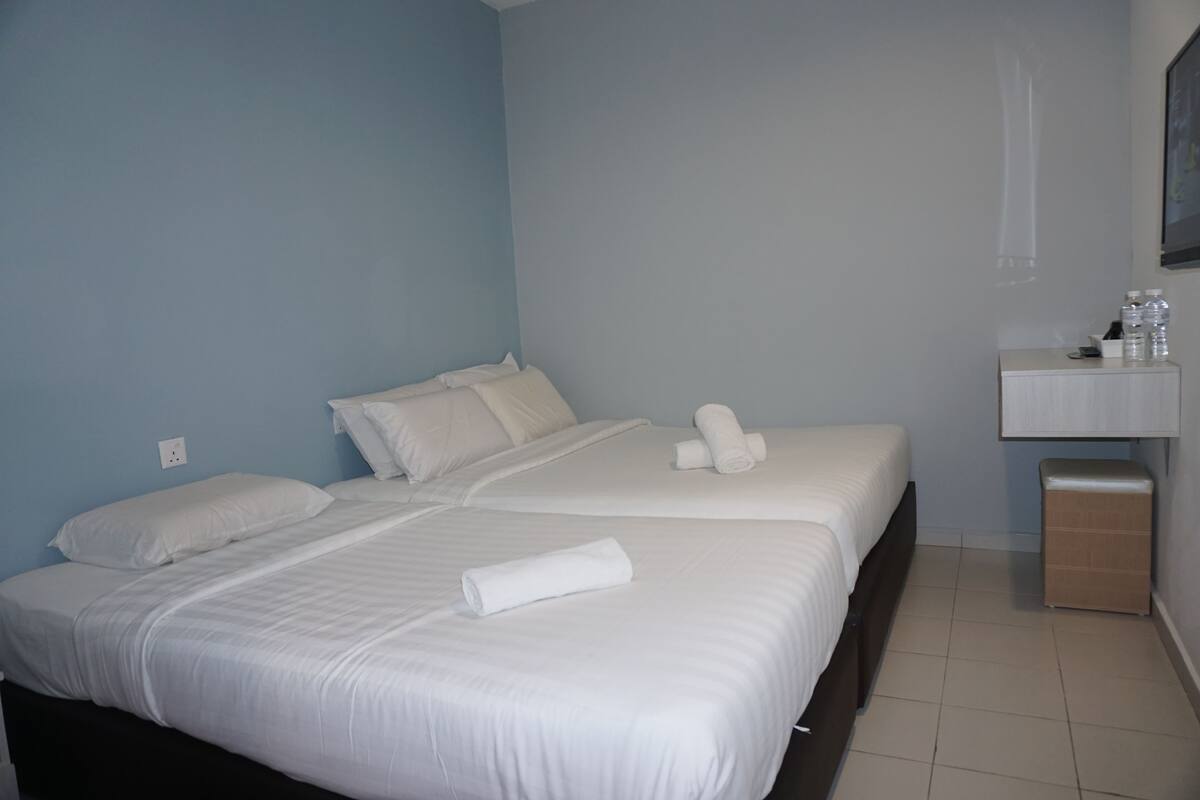 Hotelkamer met twee bedden, een klein nachtkastje, een spiegel en een wandplankje met toiletartikelen.