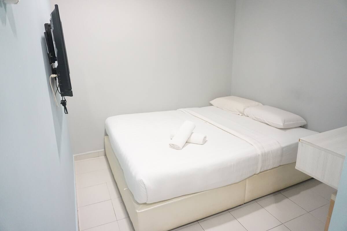 Een kamer met een enkel bed, een witte matras, kussens en een keurig opgevouwen handdoek.