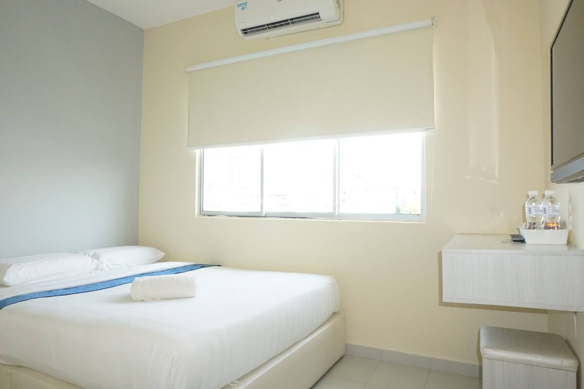 Een hotelkamer met een bed, een raam, een spiegel en een klein tafeltje met toiletartikelen.