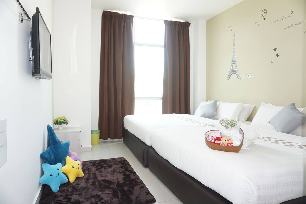 Een slaapkamer met een bed, kussens, een nachtkastje, een wandtelevisie, gordijnen, een raam en een decoratie aan de muur.