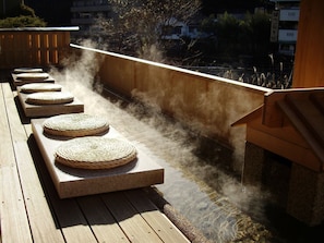 Una terraza de madera con esteras tejidas y un elemento decorativo de agua.
