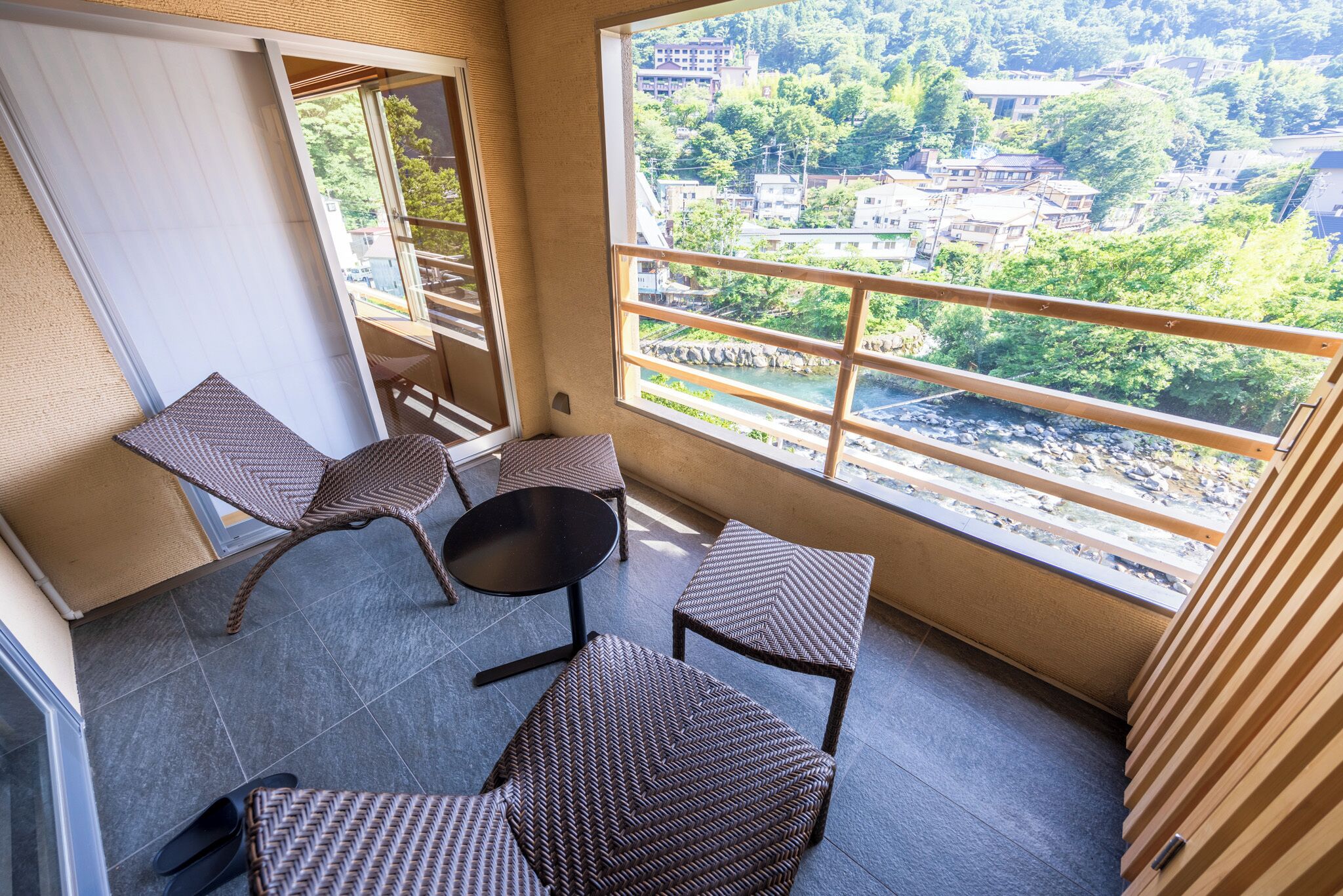 A balcony with wicker furniture, a view of a river and buildings, and a tiled floor.