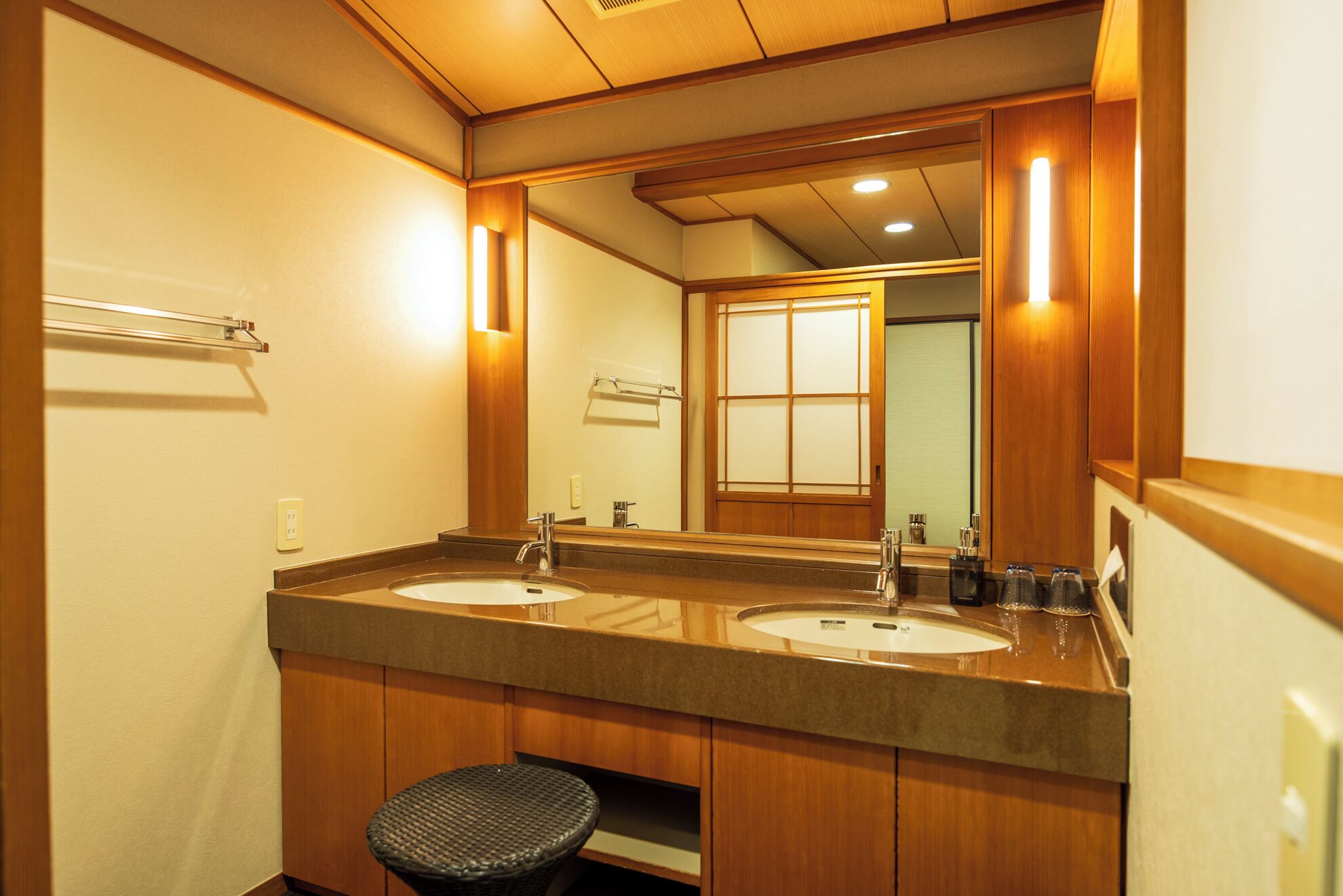 A bathroom with two sinks, a large mirror, wooden cabinetry, and a small stool.