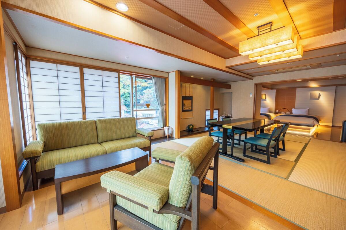 A traditional Japanese-style room with tatami flooring, a low table with chairs, a sofa, and a bed with a futon.