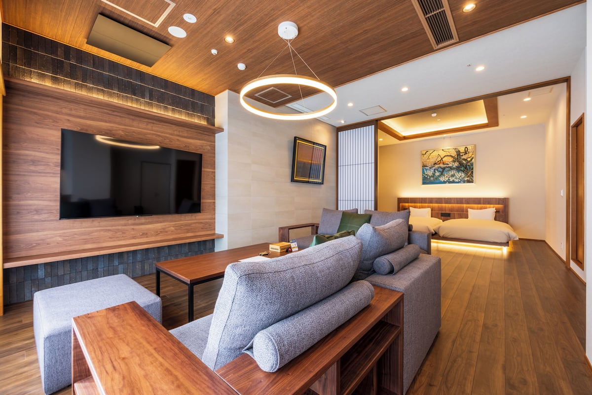 A modern hotel room with a wooden ceiling, a flat-screen TV, a sofa, a bed, and a painting on the wall.