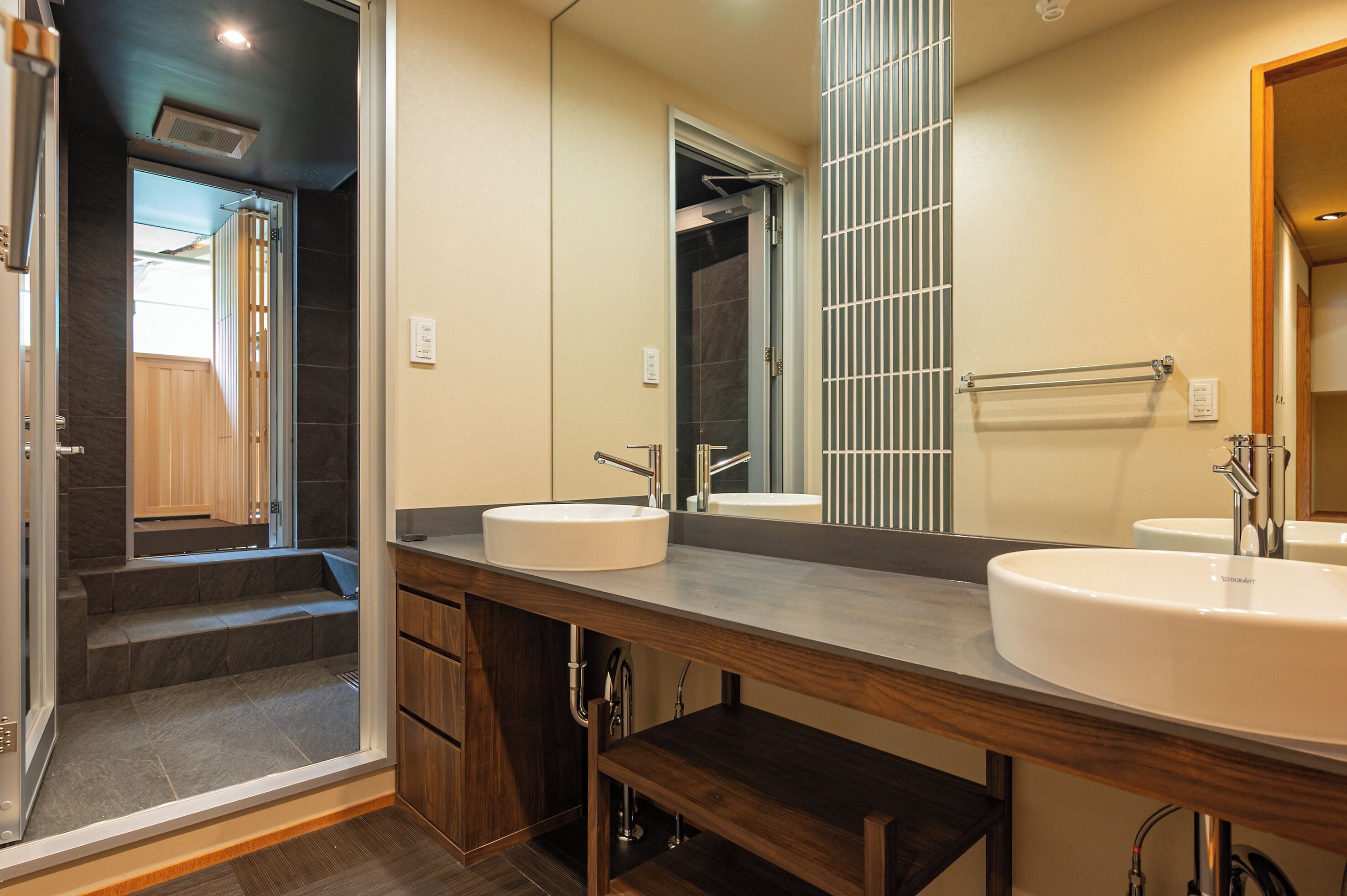 A modern bathroom with two sinks, a large mirror, and a shower area.