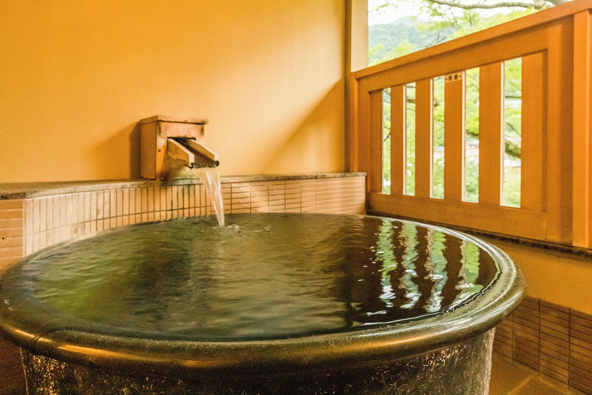 A hot tub with a wooden railing and a window with a view of greenery.
