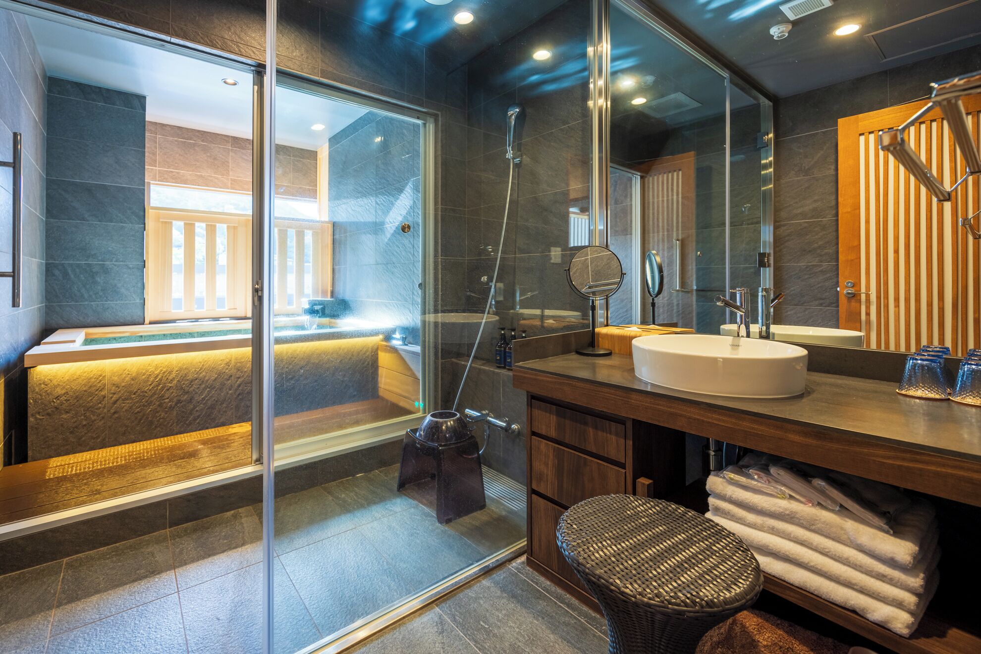Un baño moderno con ducha envuelta en vidrio, un espejo grande y un mueble de tocador de madera.