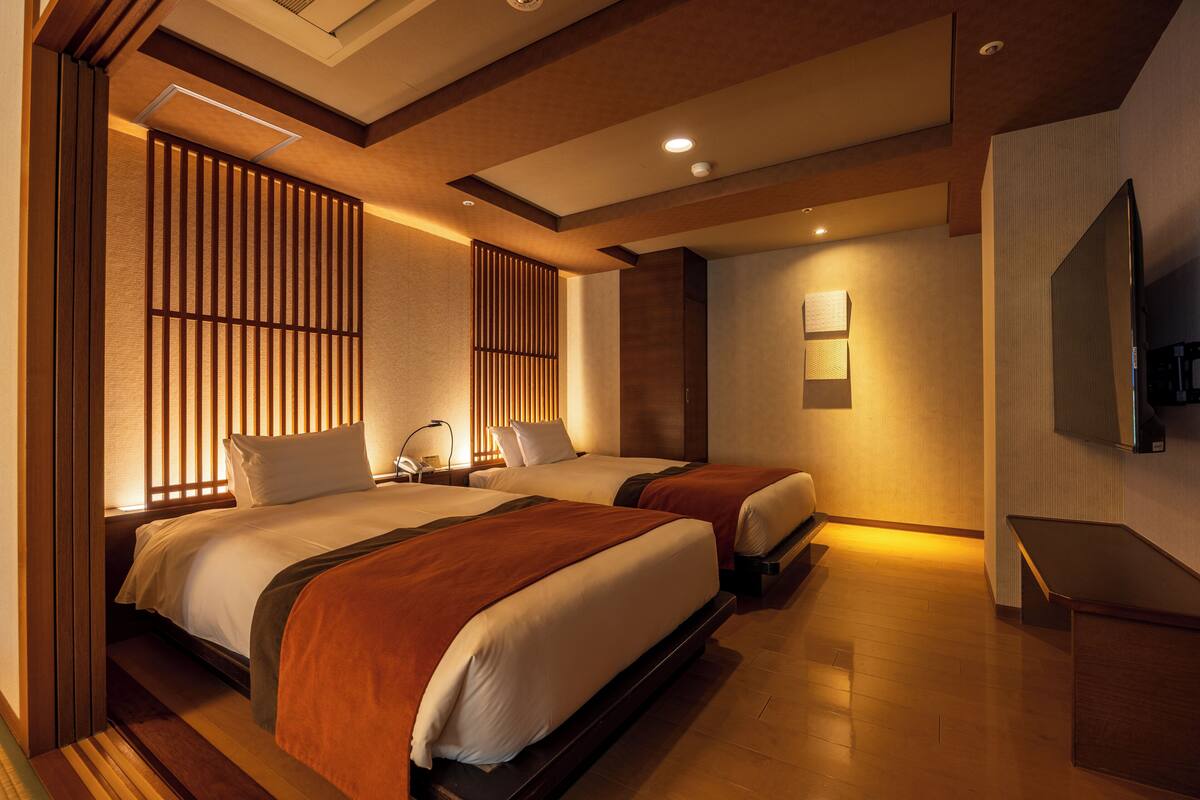 A hotel room with two beds, wooden panel dividers, a flat-screen TV, and a bench.