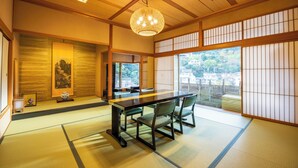 Una habitación japonesa tradicional con suelo de tatami, una mesa baja con sillas, un candelabro colgante y paneles shoji.