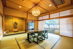 Una habitación japonesa tradicional con suelo de tatami, una mesa baja con sillas, un candelabro colgante y paneles shoji.