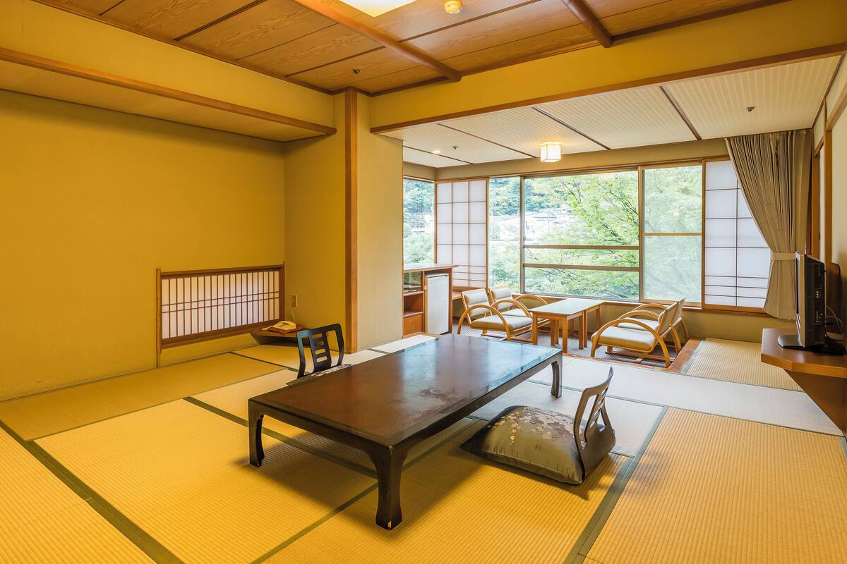 A traditional Japanese room with tatami flooring, a low table, and a view of greenery outside.