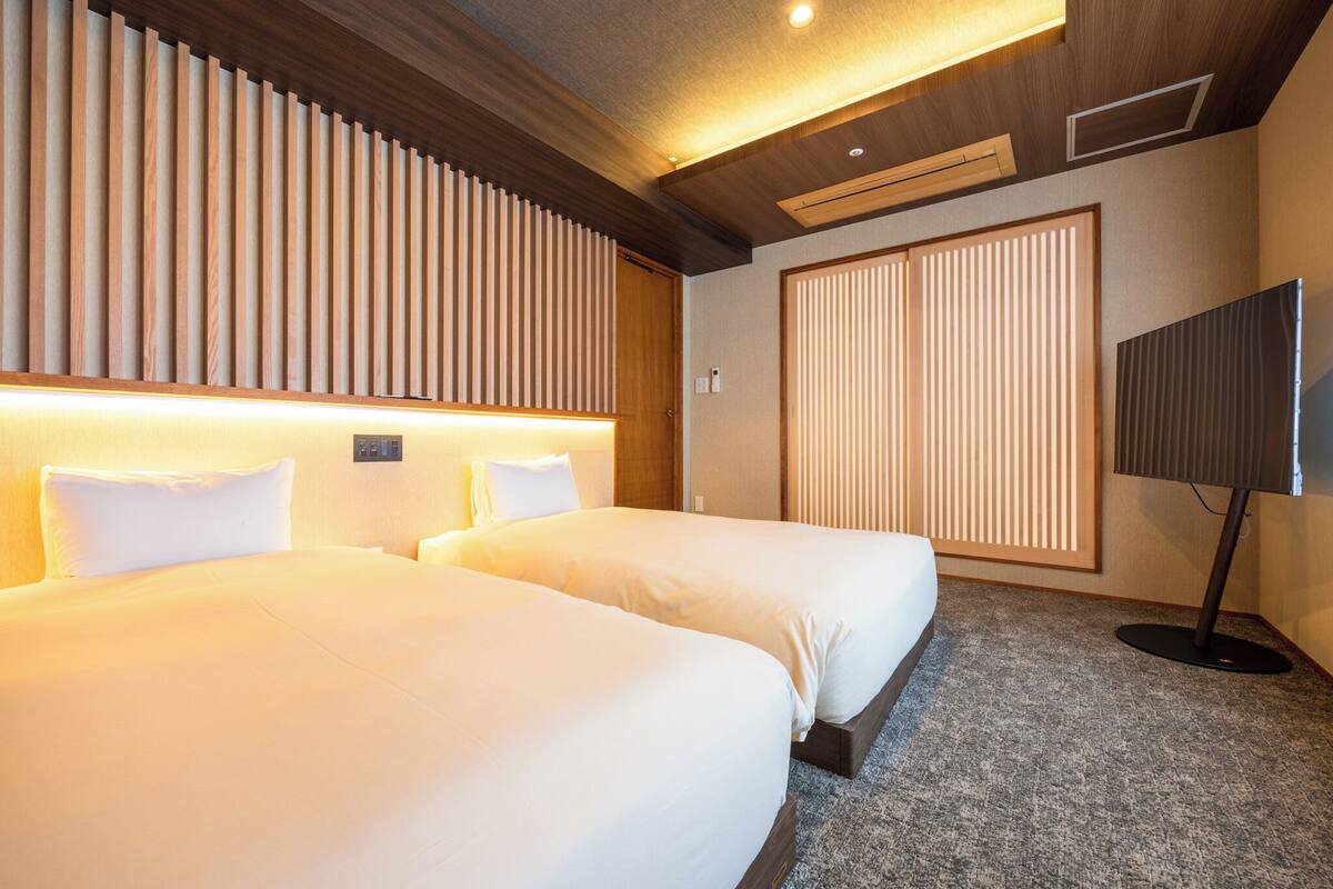A hotel room with two beds, a television, and a sliding door.