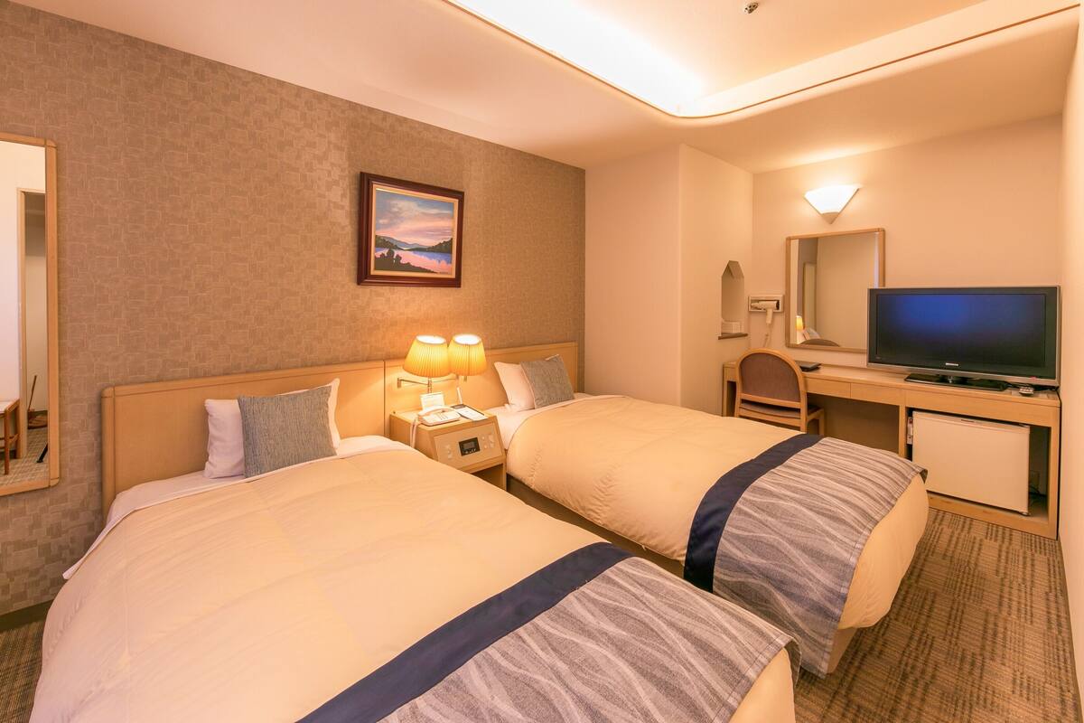 A hotel room with two beds, a desk with a TV, and a mirror.