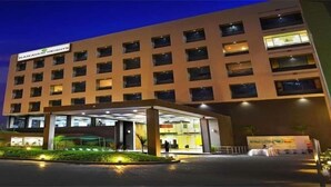Un hotel de varios pisos con fachada plana, vestíbulo cubierto y zona ajardinada.