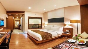 Una habitación de hotel con una cama grande, un escritorio con silla, televisión y una mesa de comedor con un jarrón de flores.