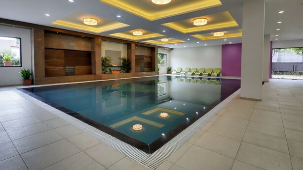 Piscina interior moderna con superficie de agua cristalina, rodeada por un suelo de baldosas e iluminación empotrada en el techo.