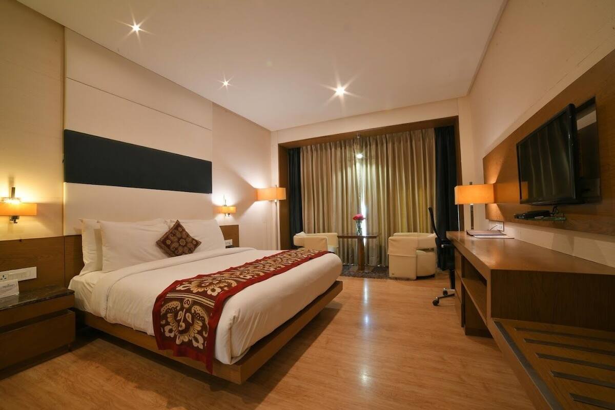 Une chambre d’hôtel avec un grand lit, des tables de chevet, un bureau, une chaise, une télévision et des rideaux.
