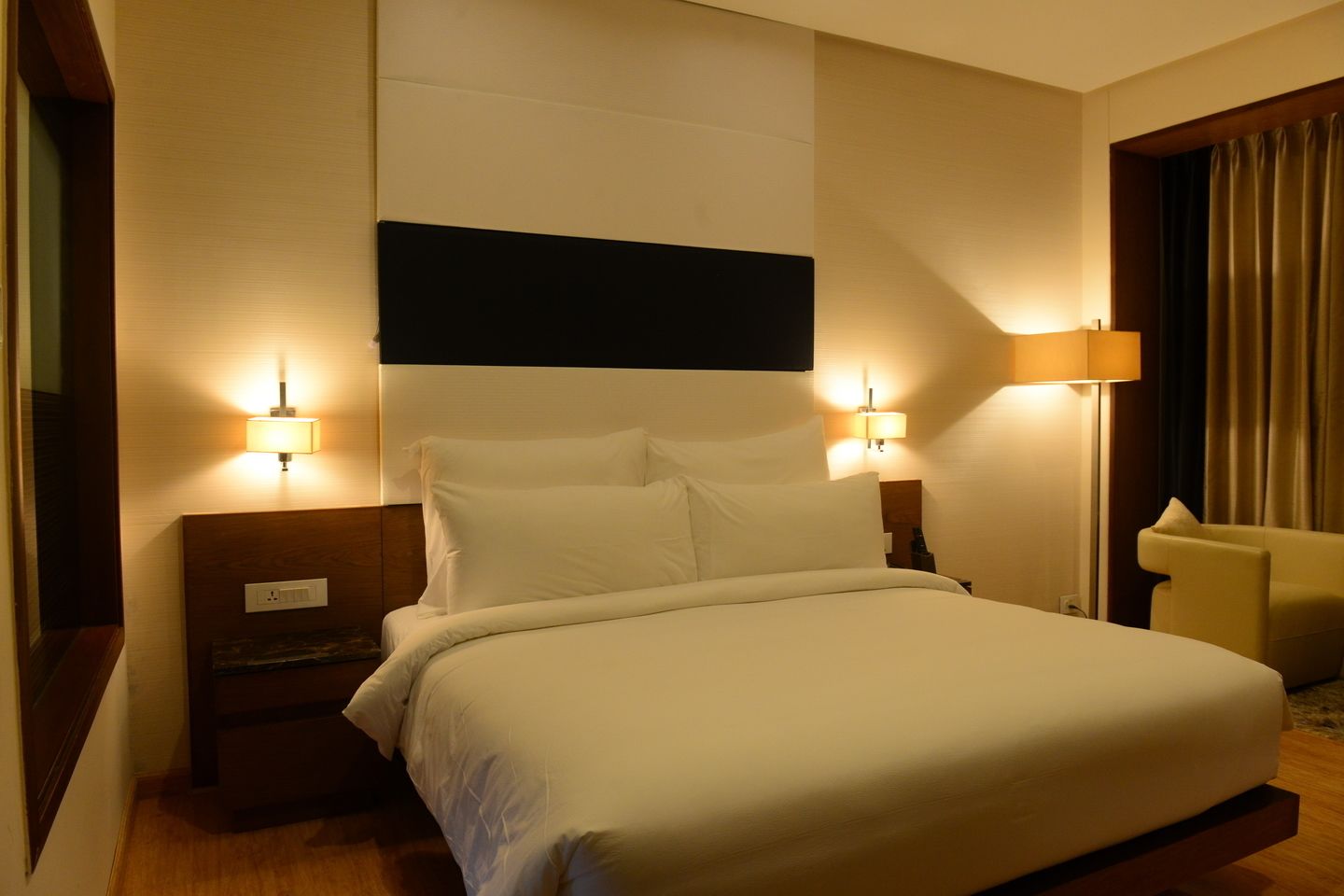 A hotel room with a large bed, two bedside tables, a nightstand, a chair, and two wall-mounted lamps.