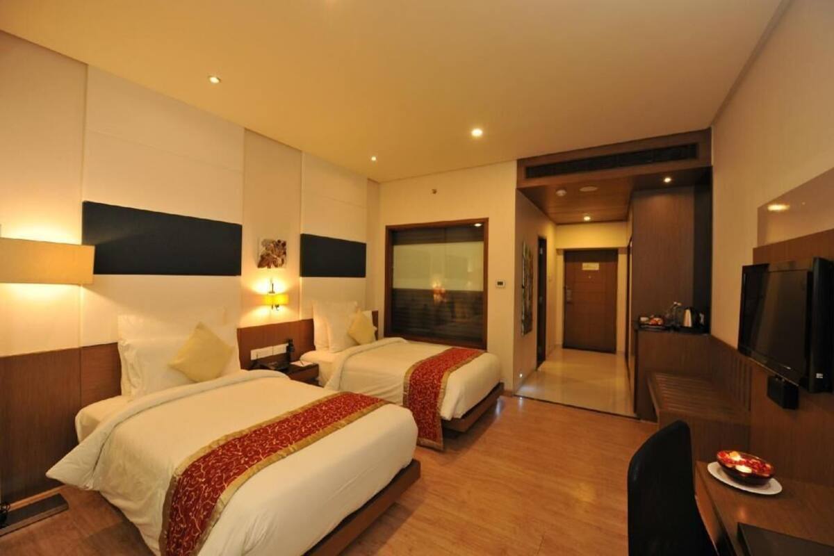 Une chambre d’hôtel avec deux lits, un bureau, une télévision et une porte donnant sur un couloir.