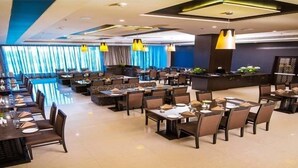 Amplia zona de comedor de hotel con varias mesas y sillas, un mostrador de recepción e iluminación moderna.