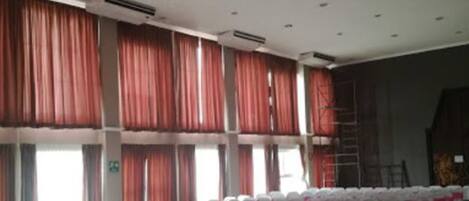 Un gran salón con filas de sillas blancas, cortinas rojas y una mesa blanca cubierta con un mantel rojo.