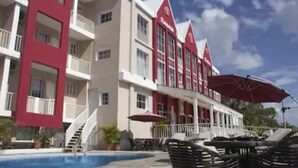 Un hotel con zona de piscina, mobiliario exterior y fachada roja y blanca.