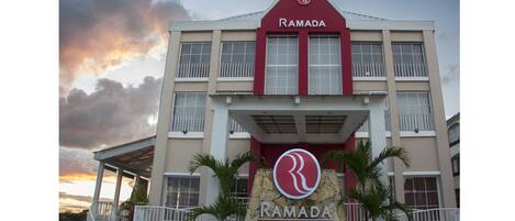 Un edificio de varios pisos con un llamativo letrero de 'RAMADA' en la entrada, que incluye un logotipo y las palabras 'WORLDWIDE LIKAL FLORES'.