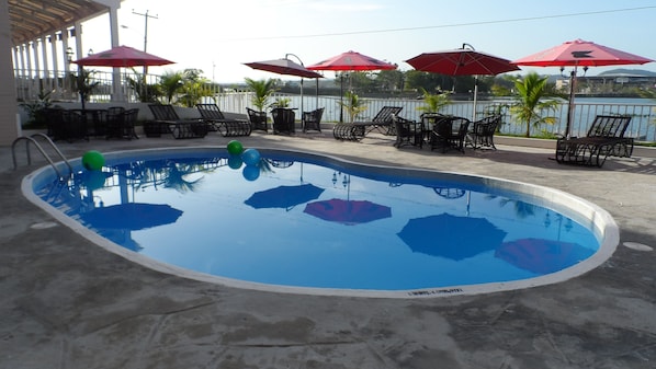 A swimming pool with lounge chairs and umbrellas, surrounded by a railing and palm trees. - Ramada Tikal Isla De Flores Hotel (Flores)