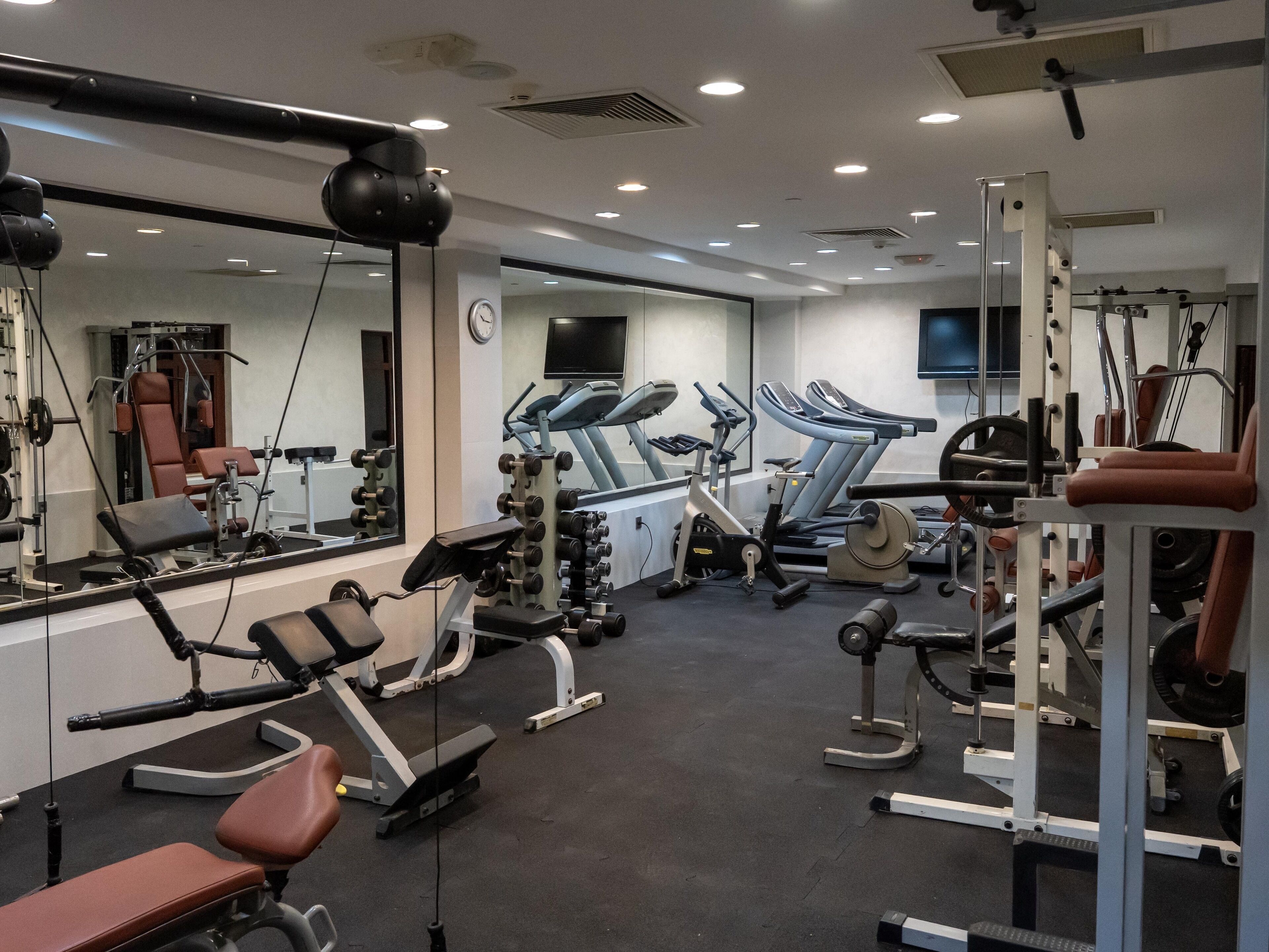 Une salle de sport équipée de matériel d’exercice, avec un miroir et une horloge au mur.