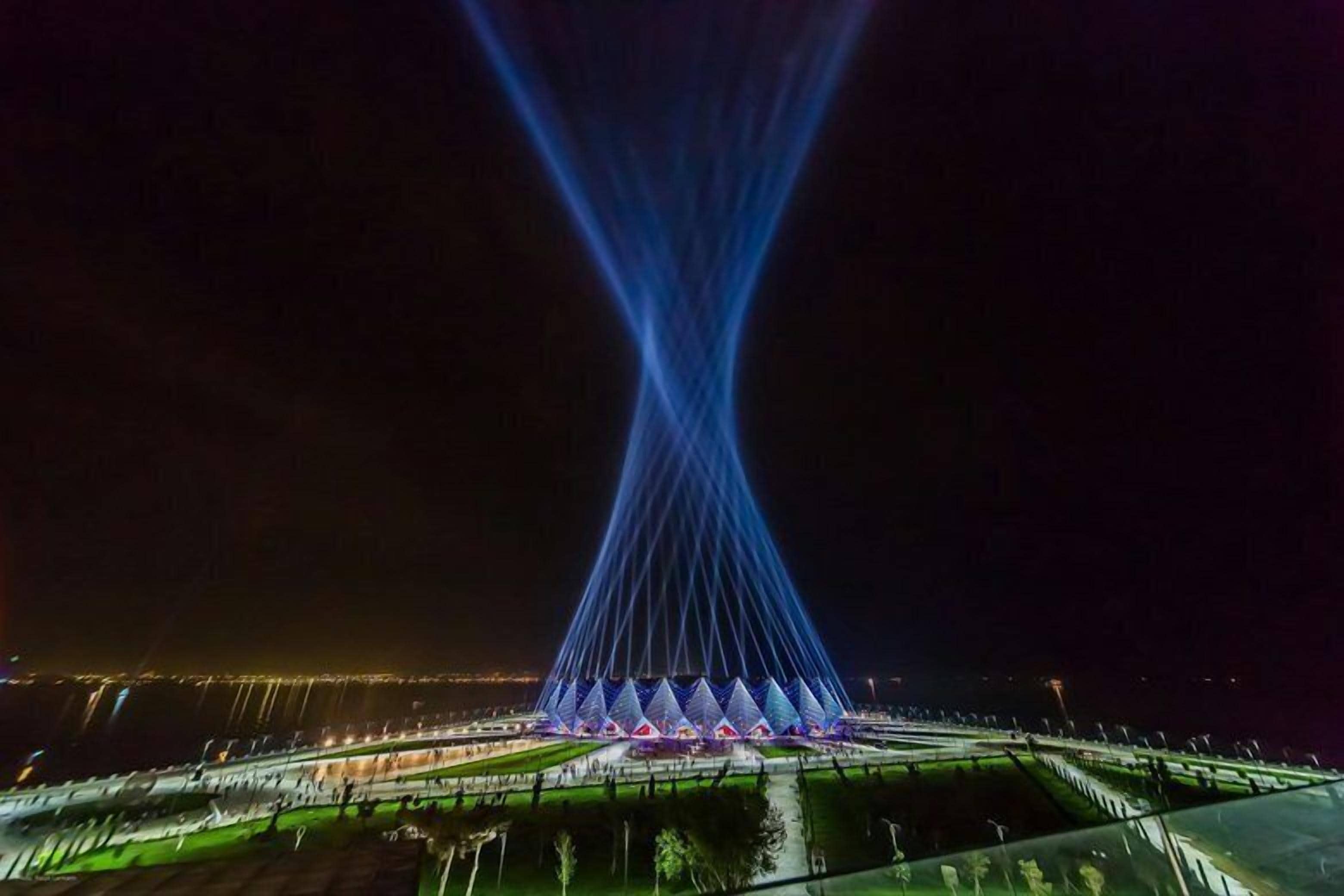 Une grande structure illuminée, dotée d’une flèche centrale et de plusieurs niveaux de plateformes triangulaires.