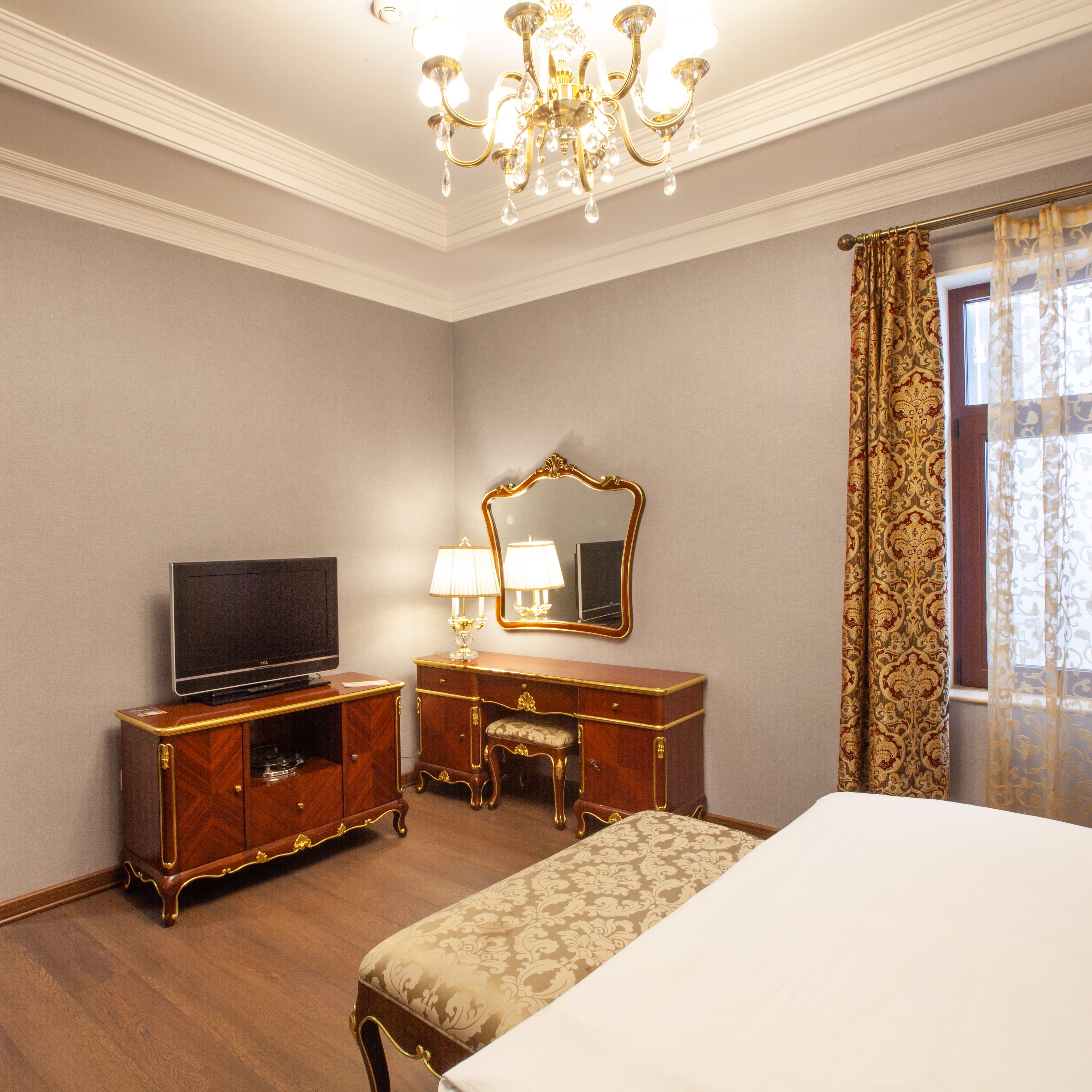 Une chambre d’hôtel avec un lit, une télévision, une commode, un miroir et un lustre.
