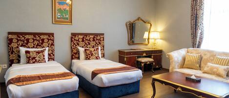 A hotel room with two beds, a desk, a sofa, a chandelier, and a large mirror.