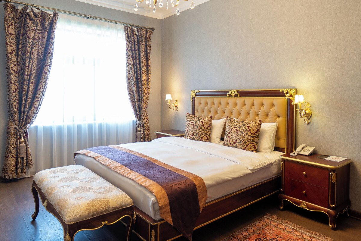 A hotel room with a large bed, a bedside table, a nightstand, and a chandelier.