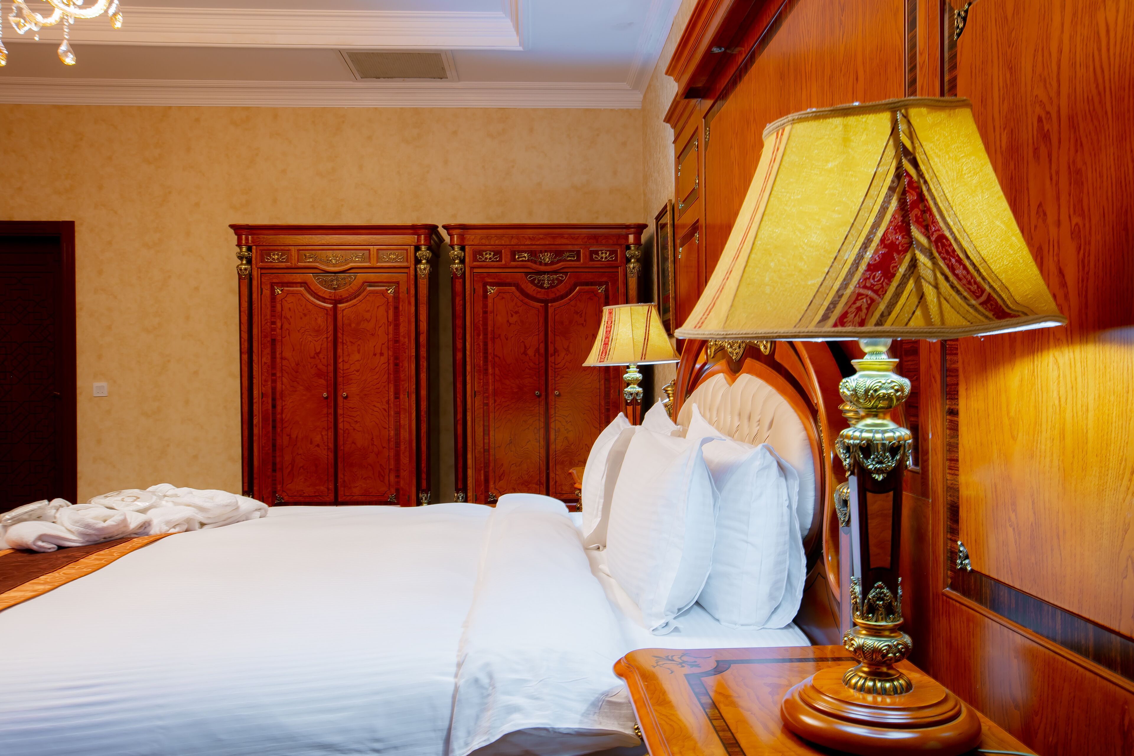 Habitación de hotel con una cama grande, armario de madera y una lámpara clásica.
