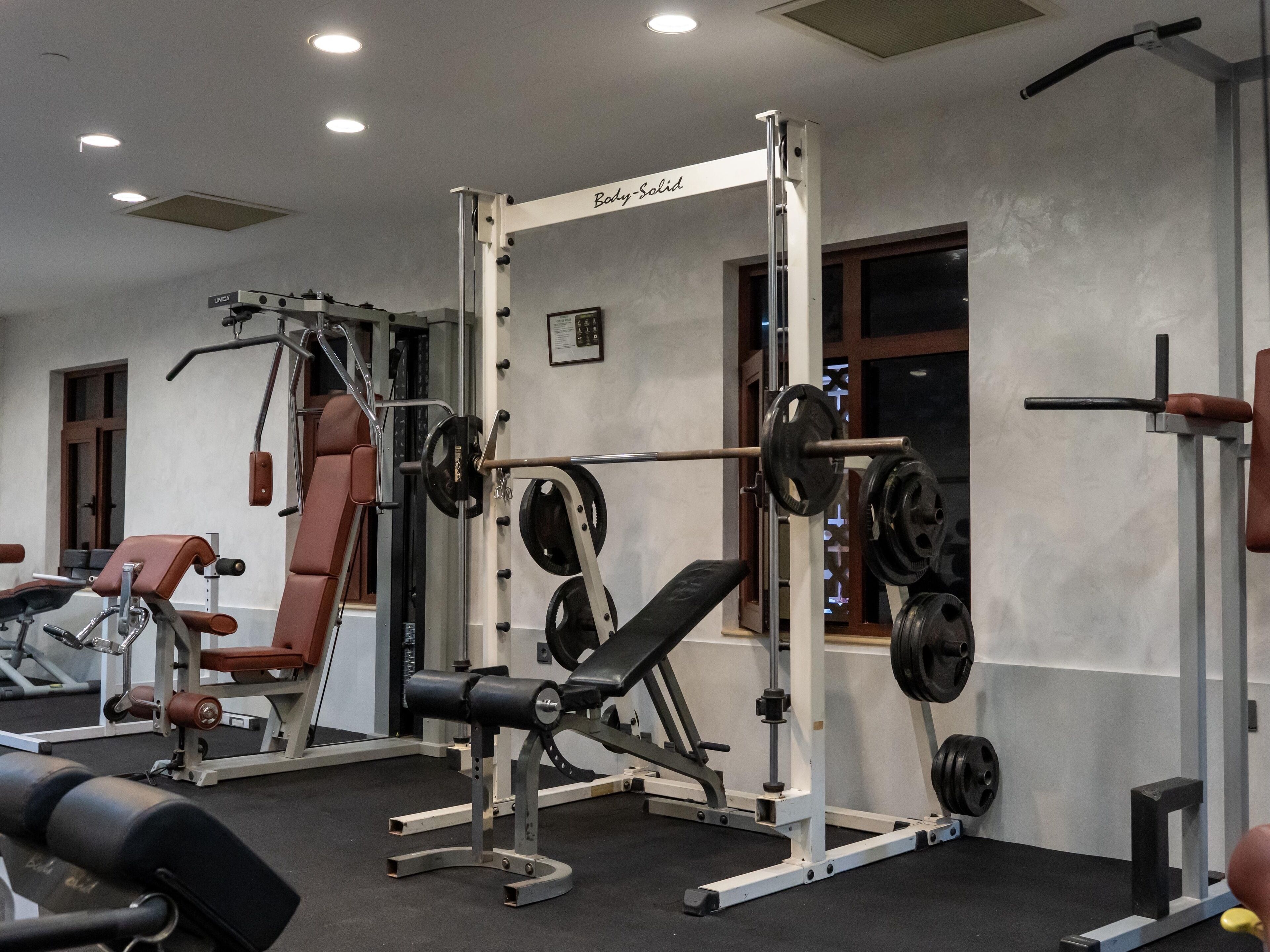 A gym with weightlifting equipment, benches, and a wall-mounted squat rack.