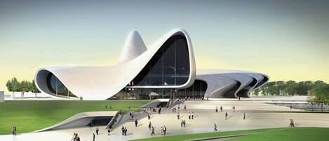 A modern architectural building with a unique curved design, surrounded by a spacious outdoor area with a water feature and greenery.